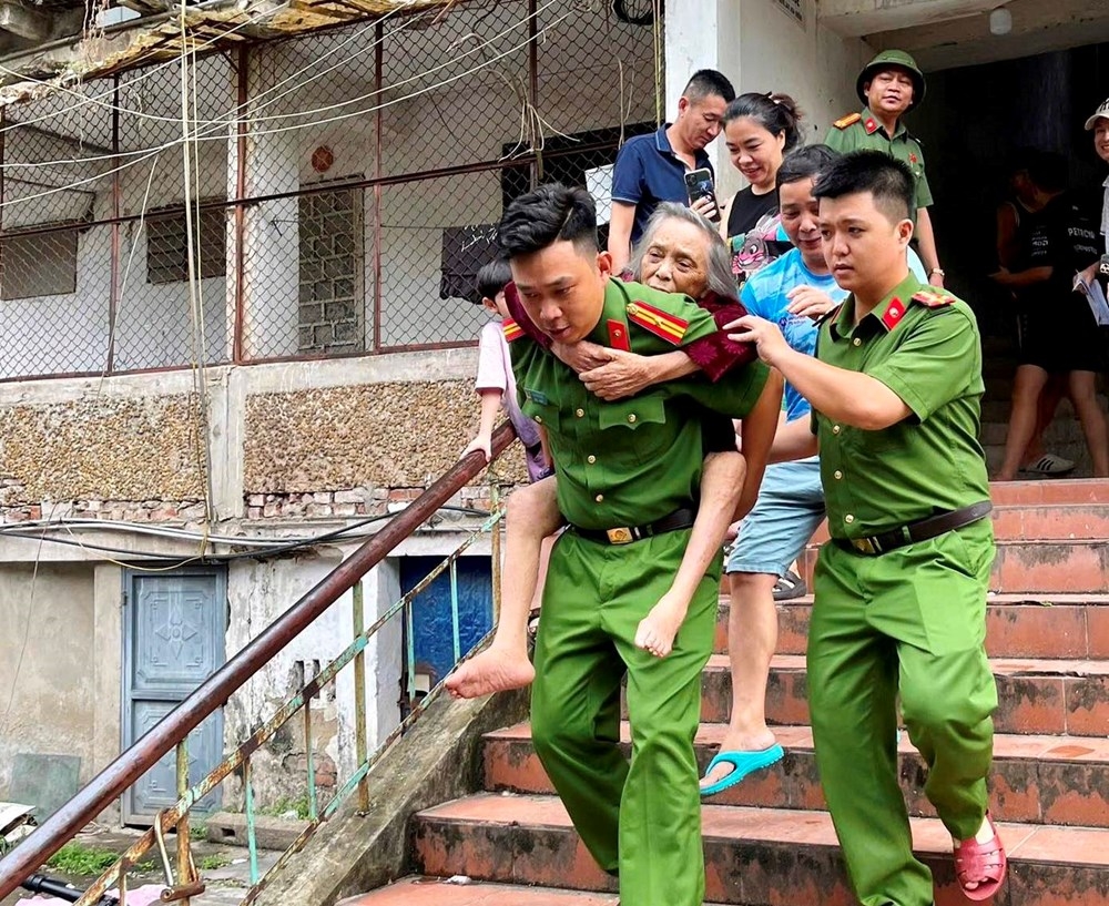 Lực lượng chức năng hỗ trợ di dời người dân sinh sống tại khu chung cư Quang Trung đến nơi tránh trú an toàn