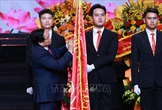 Thủ tướng Phạm Minh Chính gắn Huân chương Hồ Chí Minh lên lá cờ truyền thống của Đài Tiếng nói Việt Nam. Ảnh: TTXVN.