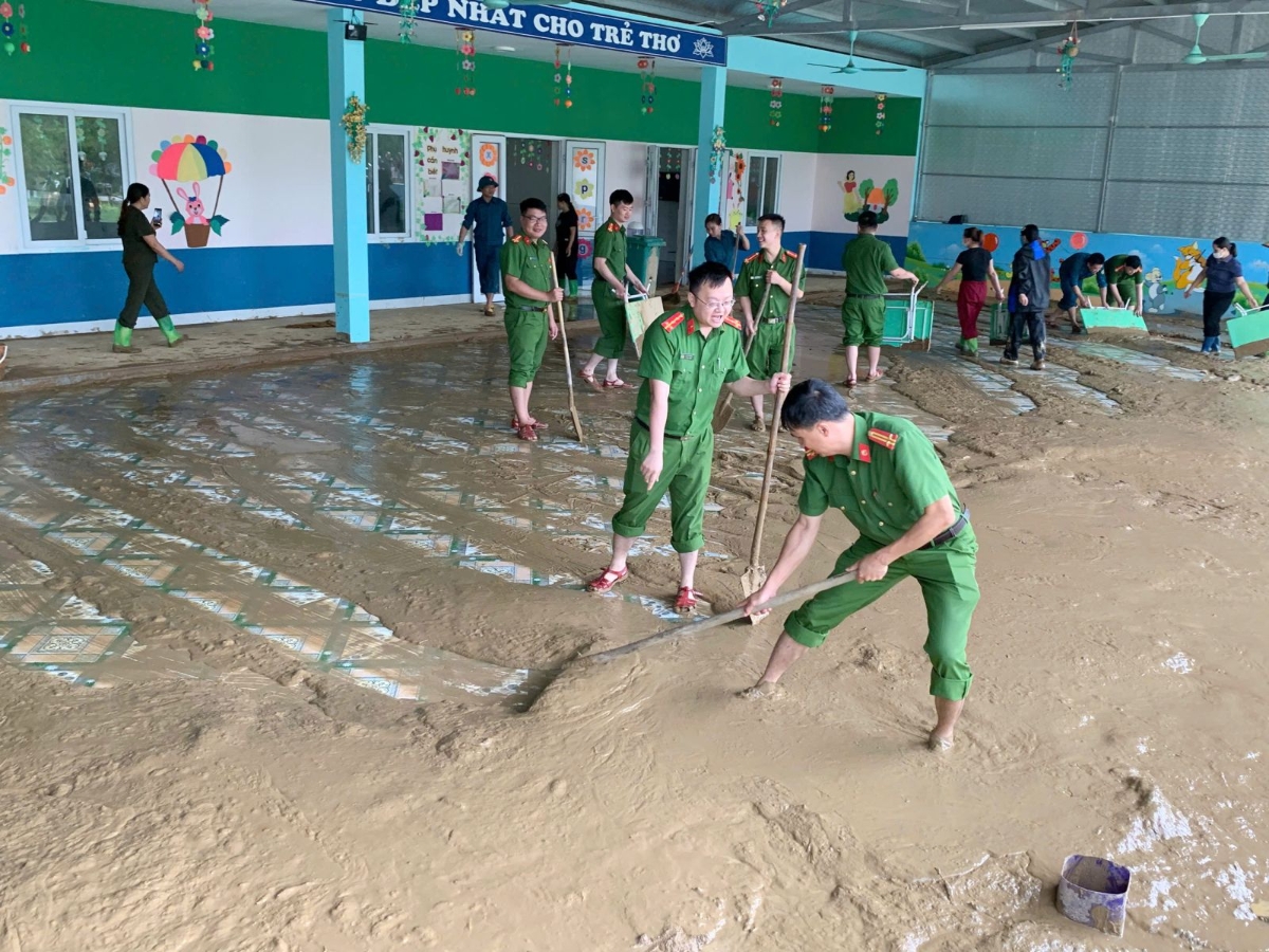 Lực lượng công an và giáo viên chung tay lau rửa bàn ghế, vệ sinh lớp học để sớm đón trẻ trở lại trường.