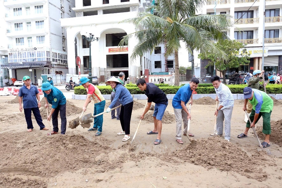 Lực lượng dân quân tự vệ phối hợp cùng người dân xúc cát, khơi thông vỉa hè bị vùi lấp.