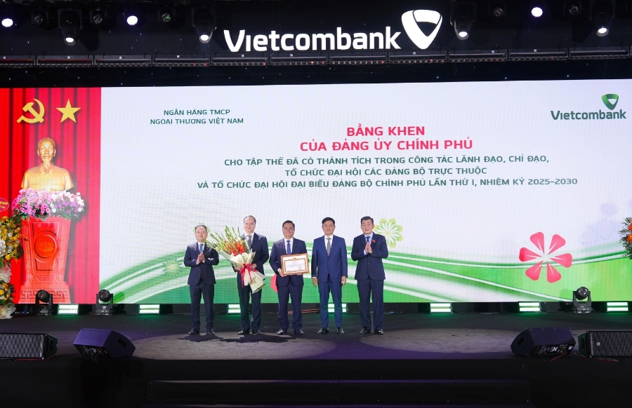 Đại diện Vietcombank, đồng chí Nguyễn Thanh Tùng - Ủy viên Ban Chấp hành Đảng bộ Chính phủ, Bí thư Đảng ủy, Chủ tịch HĐQT; đồng chí Lê Quang Vinh - Phó Bí thư Đảng ủy, Thành viên HĐQT, Tổng giám đốc; đồng chí Nguyễn Danh Phương - Phó Bí thư thường trực Đảng ủy nhận bằng khen của Đảng ủy Chính phủ với thành tích trong công tác lãnh đạo đã tổ chức đại hội các Đảng bộ trực thuộc và tổ chức Đại hội đại biểu Đảng bộ Chính phủ lần thứ nhất nhiệm kỳ 2025-2030. Đồng chí Nguyễn Đức Phong - Phó Bí thư chuyên trách Đảng ủy Chính phủ (ngoài cùng bên phải) trao tặng bằng khen và đồng chí Nguyễn Ngọc Cảnh - Ủy viên BTV Đảng ủy, Phó Thống đốc NHNN (ngoài cùng bên trái) tặng hoa chúc mừng.