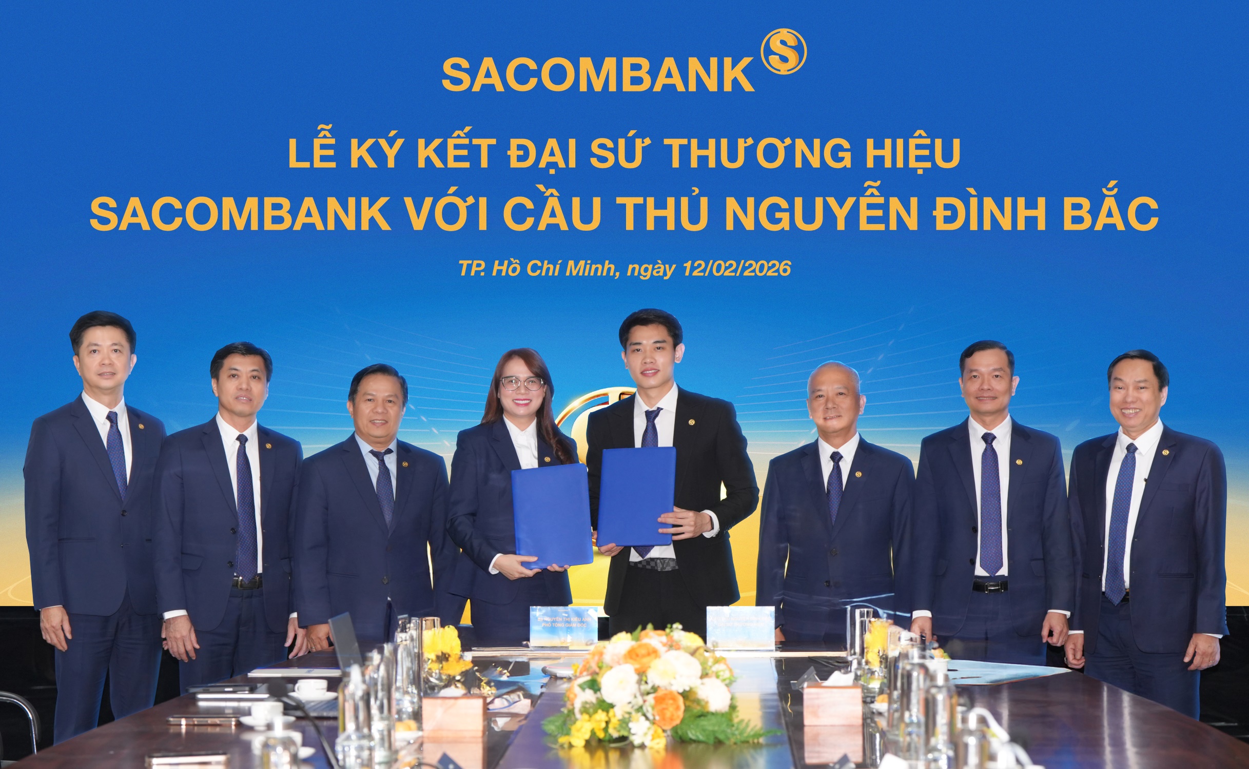Cầu thủ Nguyễn Đình Bắc (phải) và bà Nguyễn Thị Kiều Anh (trái) - Phó Tổng giám đốc SACOMBANK thực hiện nghi thức ký kết Thỏa thuận Đại sứ thương hiệu dưới sự chứng kiến của Ban lãnh đạo Ngân hàng. Ảnh: SACOMBANK.