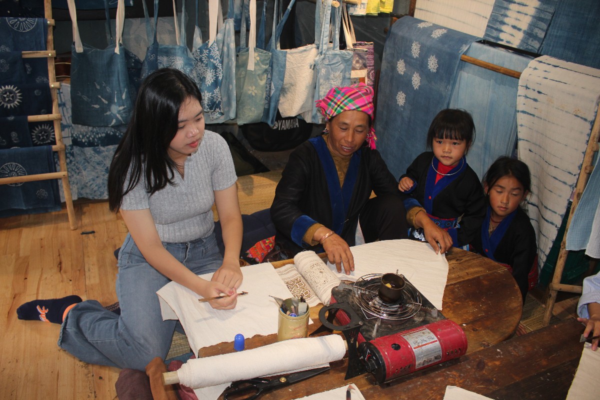 Bà Vàng Thị Mì trình diễn vẽ các hoa tiết hoa văn của người Mông lên vải trước khi nhuộm chàm. Ảnh: Chu Khôi.