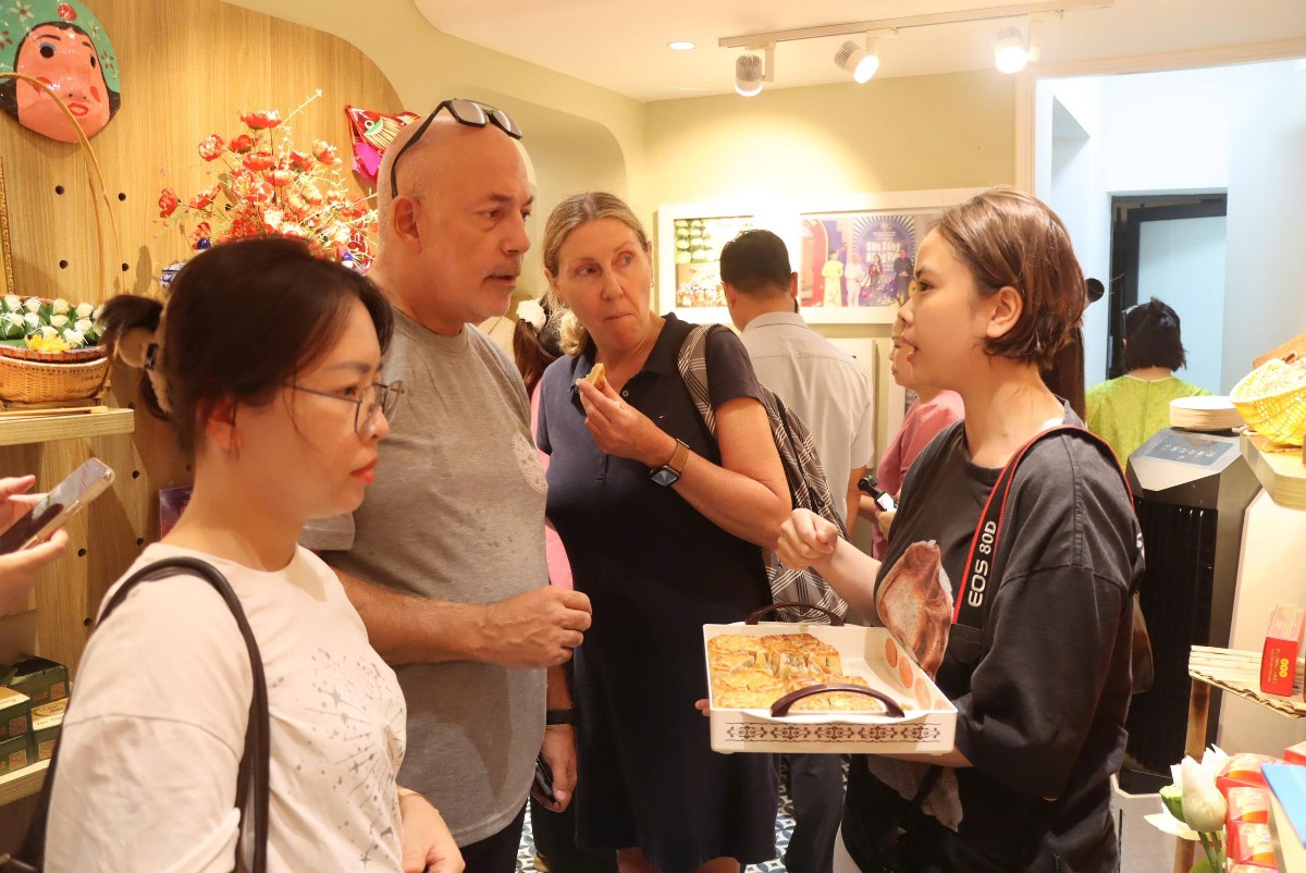 Du khách nước ngoài nếm thử bánh trung thu của Hộ kinh doanh Phương Soát được trưng bày tại 62 Tràng Tiền - Ảnh: Song Hà.