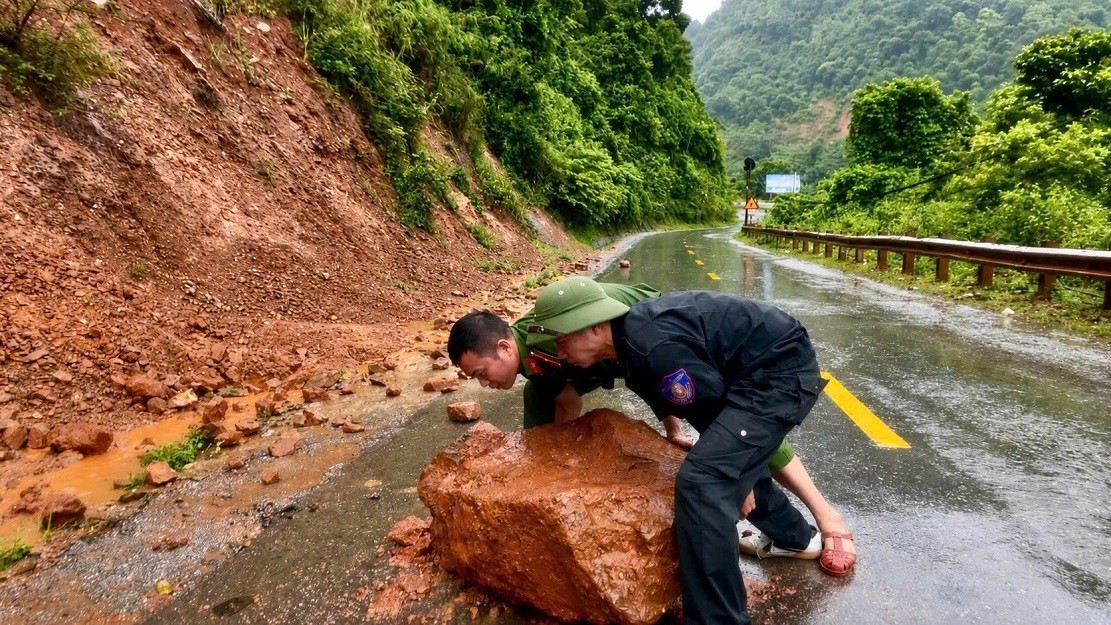 Cán bộ, chiến sĩ Công an xã Nậm Cắn khẩn trương di chuyển tảng đá cùng đất đá ra khỏi mặt đường, góp phần bảo đảm giao thông thông suốt, an toàn. Ảnh: Công an Nghệ An