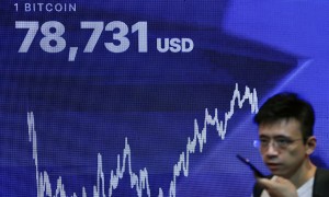 Một người đàn ông đi ngang qua màn hình hiển thị giá Bitcoin theo thời gian thực tại hội nghị Bitcoin Asia ở Hồng Kông vào ngày 27/8/2026. Ảnh: Reuters